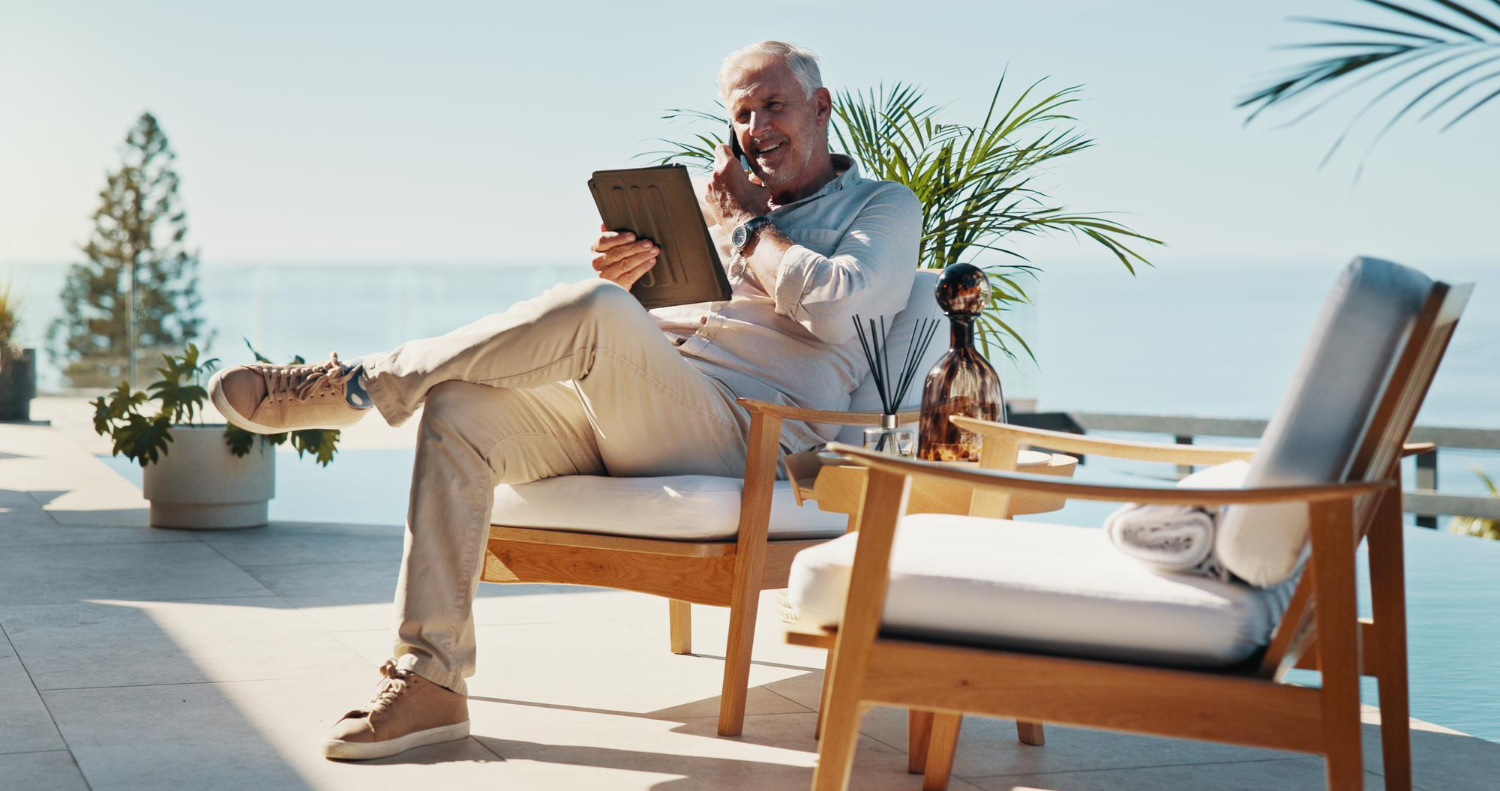 Older man using a tablet on a terrace beside the water